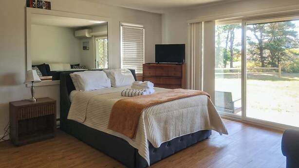 A bedroom with a bed, a TV, a dresser, a mirror, and a window. - Cozy, Ground-Floor Getaway w/ Free WiFi, a Kitchen, Shared Pool, & Private Patio (North Truro)