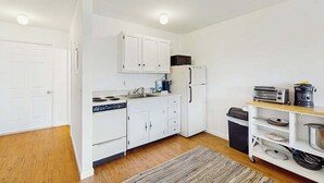 A compact kitchen with white cabinets, a microwave, a toaster, and a small refrigerator. - Cozy, Ground-Floor Getaway w/ Free WiFi, a Kitchen, Shared Pool, & Private Patio (North Truro)