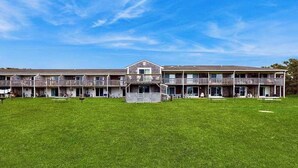 A multi-story hotel with a central courtyard, balconies, and a grassy lawn. - Cozy, Ground-Floor Getaway w/ Free WiFi, a Kitchen, Shared Pool, & Private Patio (North Truro)