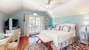 Un dormitorio con cama, televisor, escritorio y ventana con cortinas.