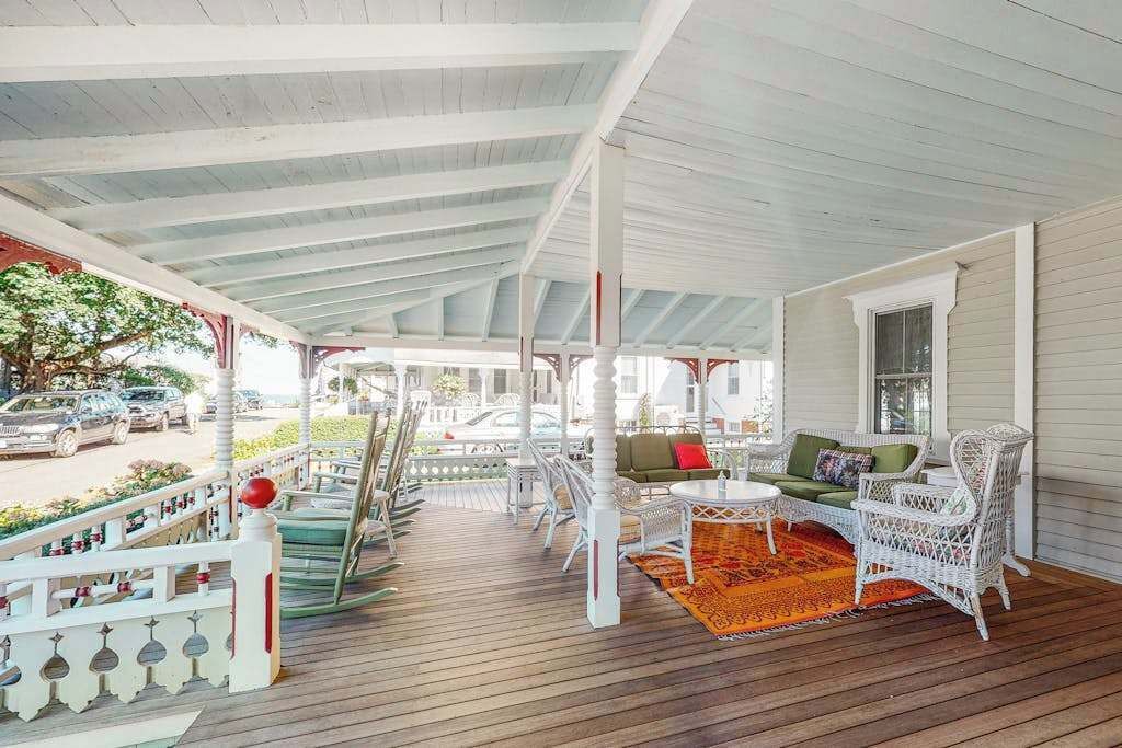 A covered porch with wicker furniture, a wooden floor, and a white railing.