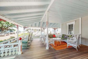 Een overdekte veranda met rieten meubilair, een houten vloer en een witte balustrade.