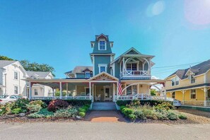 Ein zweistöckiges Haus mit Veranda, einem kleinen Turm und einem Vorgarten mit Pflanzen.