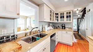 Una cocina con armarios blancos, encimera de granito, electrodomésticos de acero inoxidable y suelo de madera.