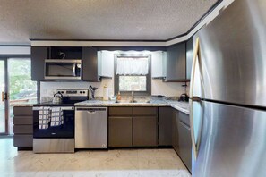 A modern kitchen with stainless steel appliances, a dishwasher, and a window with a white curtain.