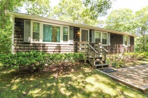 A single-story house with a front porch, a staircase leading to the entrance, and a small front yard with a wooden deck.