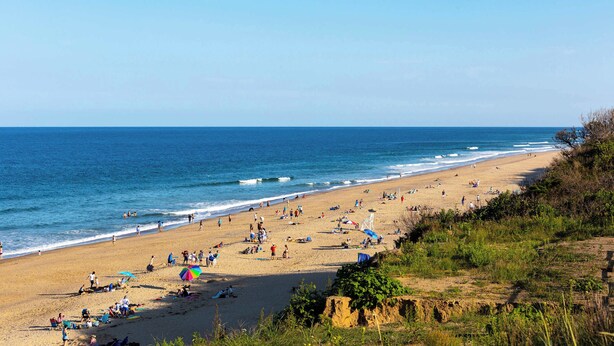 Ein Strand mit Menschen, Sonnenschirmen und blauem Himmel.