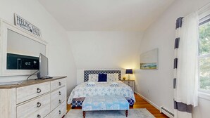 Una camera da letto con un letto, una cassettiera, una televisione e un quadro appeso al muro.