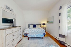 Ein Schlafzimmer mit einem Bett, einem Schminktisch, einem Fernseher und einem Bild an der Wand.