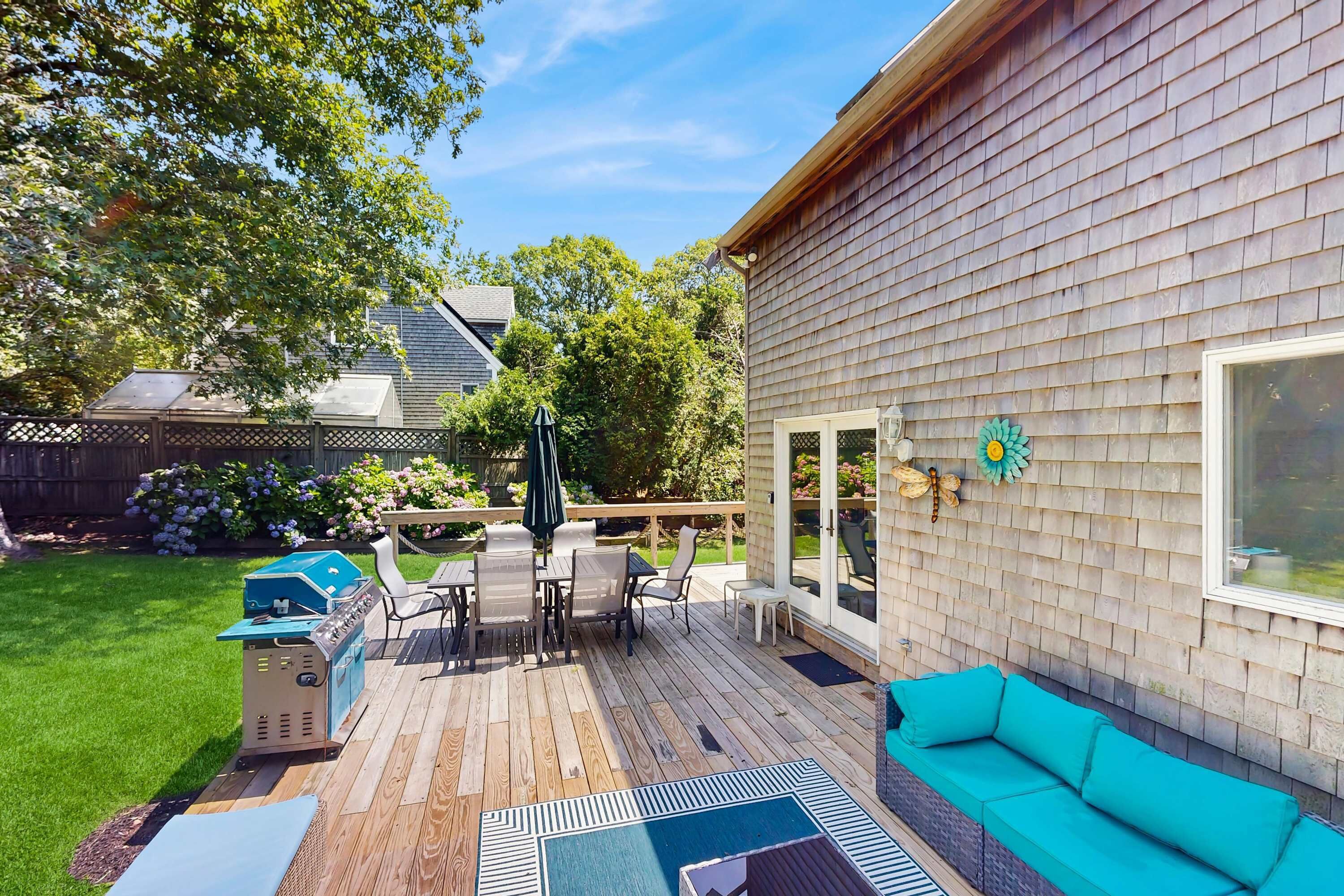 A wooden deck with outdoor furniture, a grill, and a patio area with a view of the backyard.