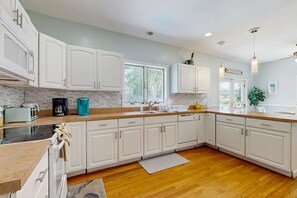 A modern kitchen with white cabinets, a large window, and a wooden floor. - Newly remodeled home w/ new furniture, large yard & great porches (Oak Bluffs)