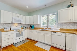 A modern kitchen with white cabinetry, a built-in microwave, a stove, and a large window providing natural light. - Newly remodeled home w/ new furniture, large yard & great porches (Oak Bluffs)
