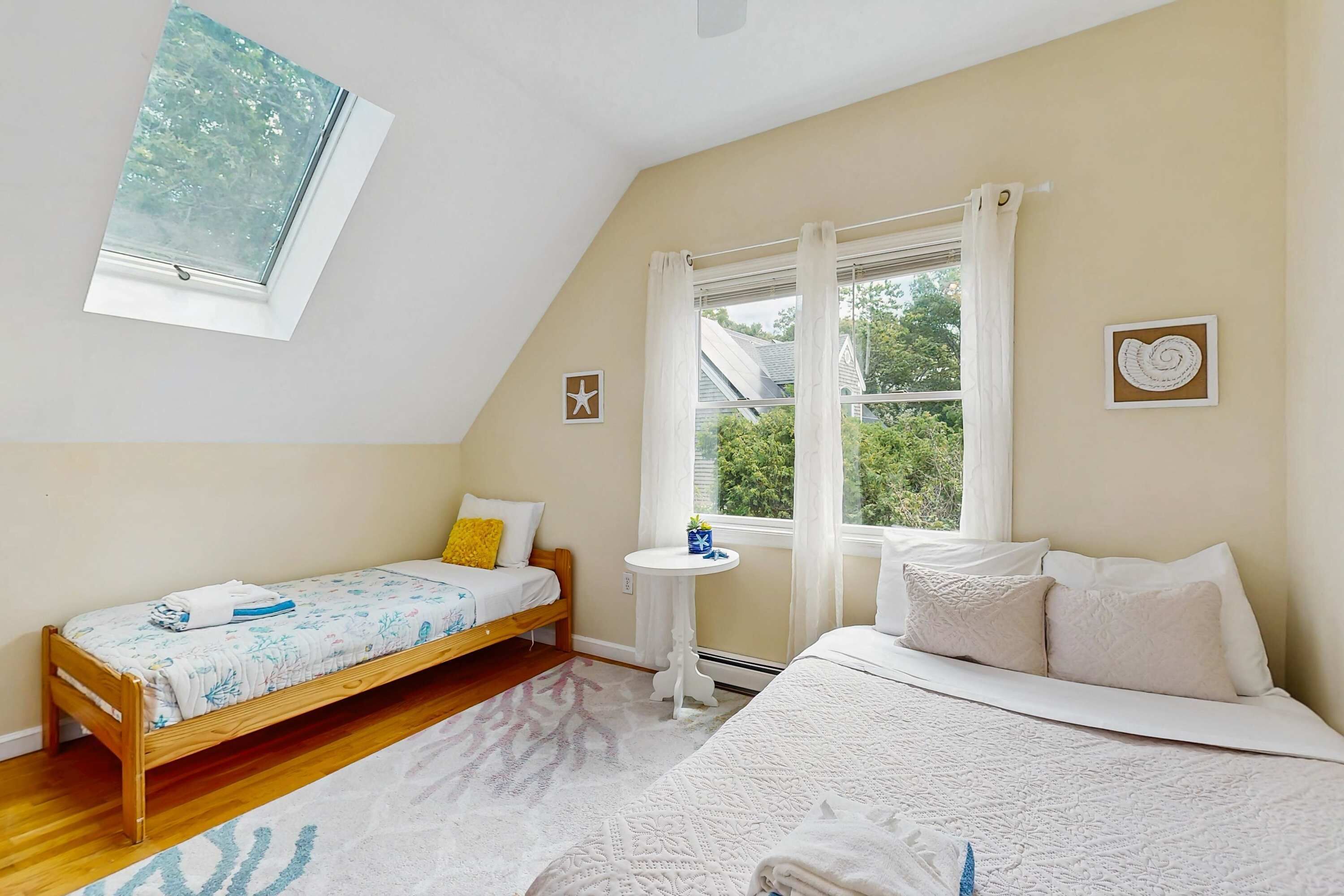Une chambre avec un plafond en pente, un lit, un petit lit, une fenêtre et une étagère fixée au mur.