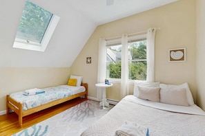 A bedroom with a sloped ceiling, a bed, a smaller bed, a window, and a wall-mounted shelf. - Newly remodeled home w/ new furniture, large yard & great porches (Oak Bluffs)