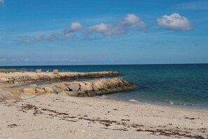 Une plage avec une digue rocheuse, un ciel bleu clair et une mer calme.