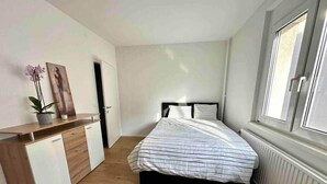 Une chambre à coucher avec un lit, une commode, une plante en pot et une fenêtre.