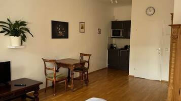 A room with a bed, a dining table with chairs, a TV, a potted plant, and a microwave in the background.