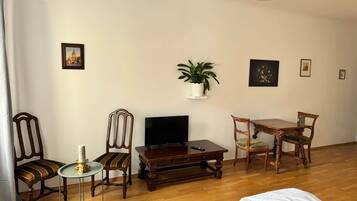 Een woonkamer met een televisie, houten meubels, een plant en kunstwerken aan de muur.