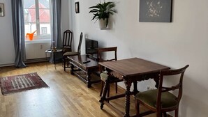Un'area pranzo con tavolo e sedie in legno, una pianta in vaso, un quadro e una vista attraverso una finestra con tende.