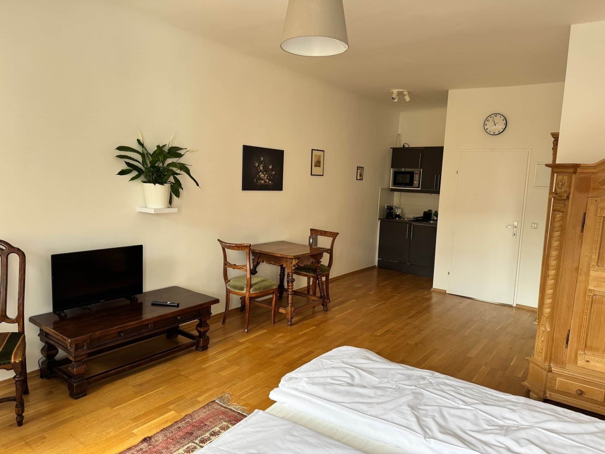 Een woonkamer met een televisie, houten meubels, een eettafel, een plant in een pot en een keuken op de achtergrond.