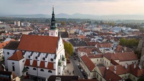 Panoramica urbana con edifici storici, una chiesa importante con guglia verde e vista libera sul paesaggio circostante.
