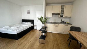 A modern bedroom with a bed, bedside table, and a small round table with a plant. Adjacent is a kitchenette with cabinets and a dining area with a table and chairs. - Cozy Studio in Vienna – Great Value Stay (Vienna)