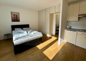 Ein Schlafzimmer mit Bett, Nachttisch, Kleiderschrank und einer Küchenzeile mit Herd.