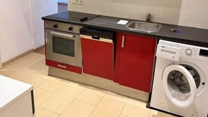 Una cucina compatta con mobili rossi, un forno in acciaio inossidabile, una lavatrice e un lavandino.