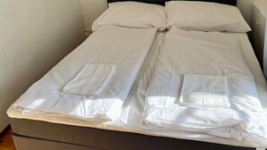 Un letto singolo con una testiera scura, biancheria da letto bianca e pavimento in legno.