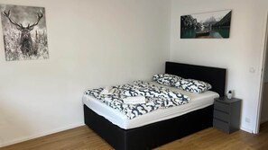 A bedroom with a black bed frame, patterned bedding, a small bedside table, and a wall-mounted picture of a deer. - Cozy Studio in Vienna – Great Value Stay (Vienna)