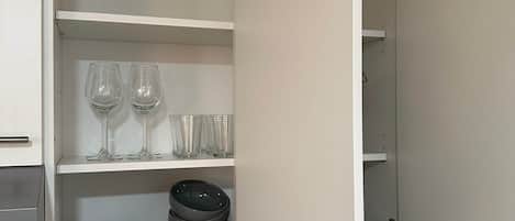 A kitchen with open cabinets, containing dishes, glasses, and utensils.