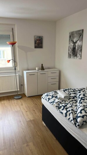 Une chambre comprenant un lit, un bureau, un radiateur, une lampe sur pied et deux œuvres d’art murales.