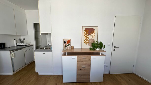 Une cuisine moderne avec des meubles blancs, un plan de travail en bois et une plante en pot.