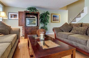 Ein Wohnzimmer mit zwei Sofas, einem Couchtisch, einem Fernseher und einer Treppe.