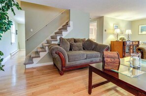 Ein Wohnzimmer mit einer Holztreppe, einem Sofa, einem Glastisch und einem Beistelltisch mit einer Lampe.