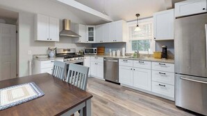 A modern kitchen with white cabinets, stainless steel appliances, a dining table with chairs, and a ceiling fan. - Peaceful perch near area's beaches with firepit, grill, streaming - dog-friendly (Harwich)