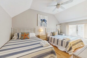 Ein Schlafzimmer mit zwei Betten, einem Deckenventilator, einem Fenster mit Jalousien und einem Bild an der Wand.