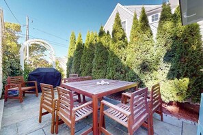 Eine Terrasse mit Holztisch und Stühlen, umgeben von hoch aufragenden immergrünen Bäumen.