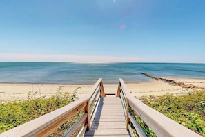 Ein Holzsteg führt zu einem Strand bei blauem Himmel.