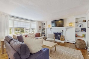 A living room with a sofa, armchair, fireplace, TV, and bookshelves. - Fantastic home near town & beach with fast WiFi, lawn games, play station & more (Hyannis)