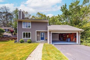 A two-story house with a garage, a front door, and a small front yard. - Dog-friendly home with great deck & association beach on Mashpee Pond (Mashpee)
