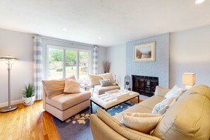 A living room with a sofa set, a coffee table, a fireplace, and a large window. - Dog-friendly home with great deck & association beach on Mashpee Pond (Mashpee)