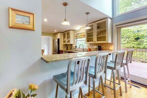 A kitchen with a bar area, stainless steel appliances, and a view of greenery outside. - Dog-friendly home with great deck & association beach on Mashpee Pond (Mashpee)