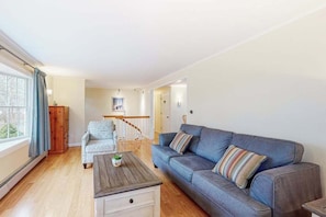 Ein Wohnzimmer mit einer Couch, einem Couchtisch, einem gemusterten Sessel und einer Treppe, die in einen anderen Raum führt.