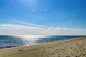 A beach with footprints leading to the water, a clear sky, and the ocean.