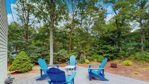 Una terrazza con poltrone Adirondack blu e un tavolo, immersa in una zona boschiva.