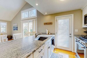 A kitchen with a granite countertop, white cabinets, a stove, and a large window.