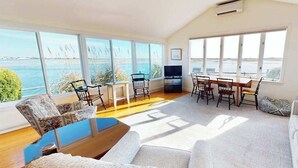 Ein geräumiges Wohnzimmer mit großen Fenstern, einem Holztisch und einem Fernseher.