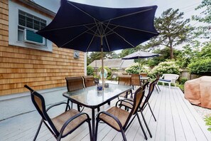 A deck with a glass-top table and chairs, surrounded by umbrellas. - Secluded ranch home with a full outdoor shower & private community beach (Brewster)