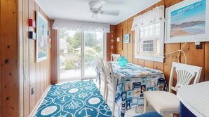 Une pièce aux murs en bois, avec un ventilateur au plafond, une table recouverte d’une nappe bleue et une vue sur l’extérieur.